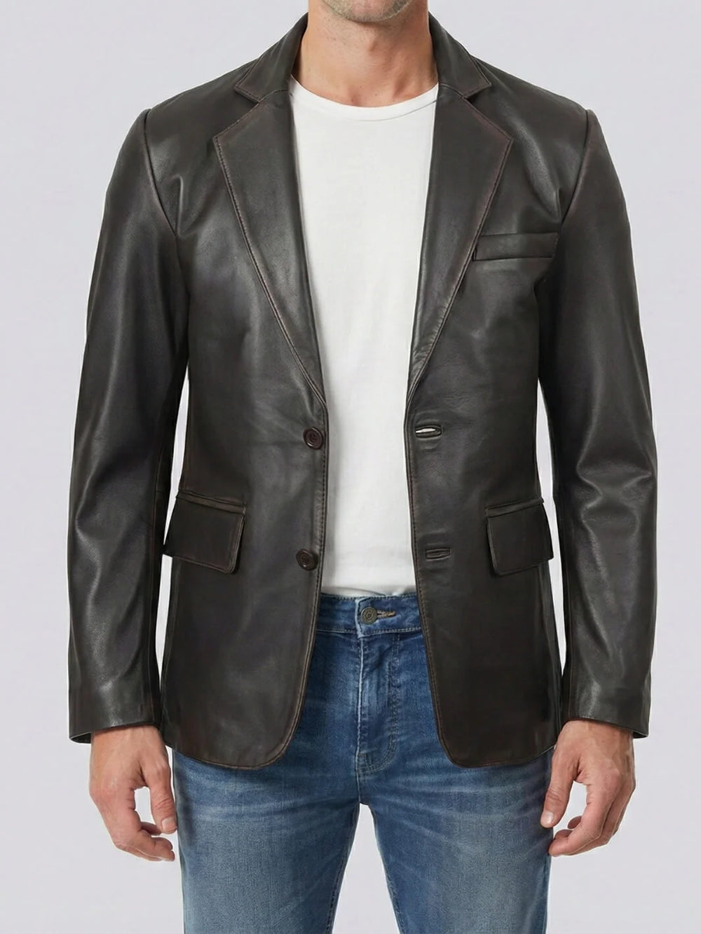 Man wearing a brown leather blazer over a white shirt and blue jeans on a light gray background